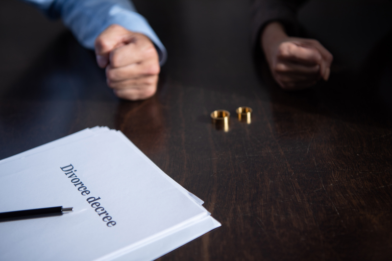 Partial view of couple at table with divorce documents and rings. Image by LightFieldStudios, Envato