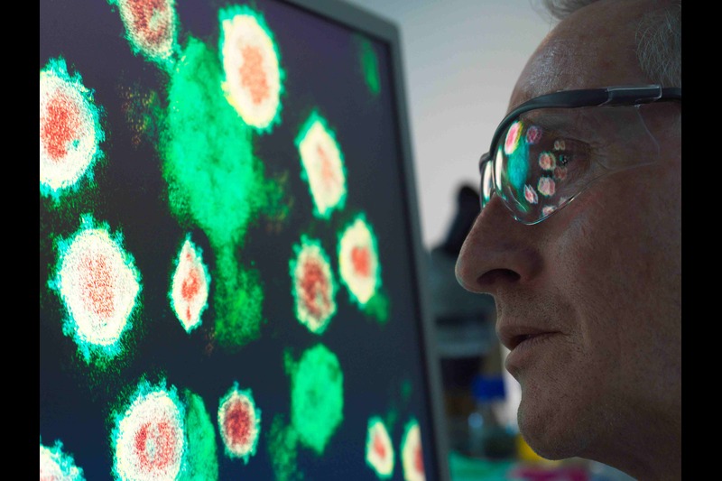 Scientist examining cells under a microscope with reflection in glasses. Credit by Image-Source, Envato